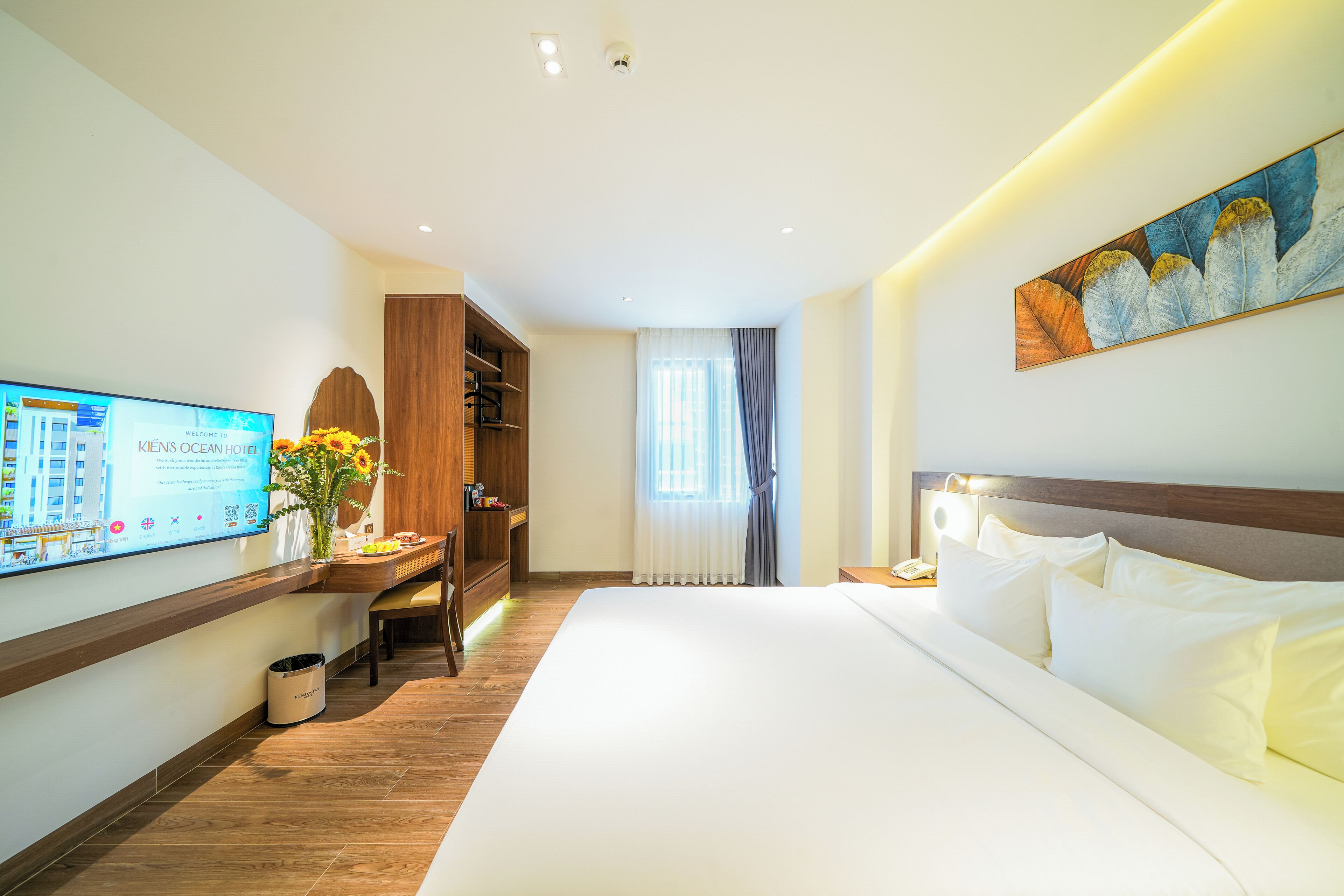 A hotel room with a bed, a desk with a computer, a wardrobe, and a painting on the wall.