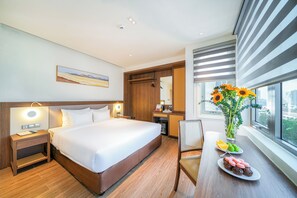 Ein Hotelzimmer mit einem großen Bett, Nachttisch, Lampe und Blick auf die Stadt durch das Fenster.