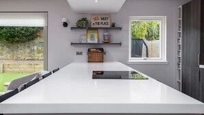 A modern kitchen with a large island, built-in shelving, and a window overlooking a garden.