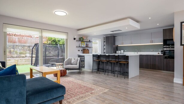 A modern kitchen with a central island, bar stools, and a dining area with a sofa and table.
