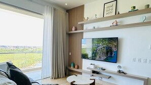 Una sala de estar moderna con un televisor grande, un sofá, una mesa de centro y vistas al exterior.