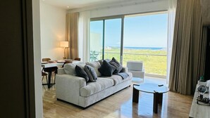 Amplia sala de estar con un sofá grande, una mesa de centro y un comedor. La habitación tiene ventanas amplias que ofrecen vistas al océano.