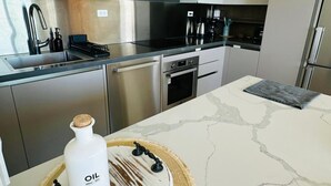 Una cocina moderna con electrodomésticos de acero inoxidable, encimera de mármol y un mantel tejido con una botella de aceite.