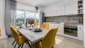 A modern kitchen with white cabinets, a built-in oven, and a dining area with a wooden table and yellow chairs.