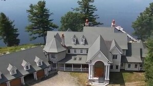 Ein großes, mehrgeschossiges Haus mit einer symmetrischen Dachlinie, einem zentralen Eingang mit Veranda und einem Steg, der ins Seeufer führt.