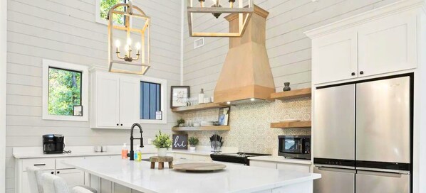 A modern kitchen with white cabinetry, a stainless steel refrigerator, a built-in microwave, and a hanging light fixture. - Hillside Vines Resort | Creekside Getaway w/Bunks (Broken Bow)