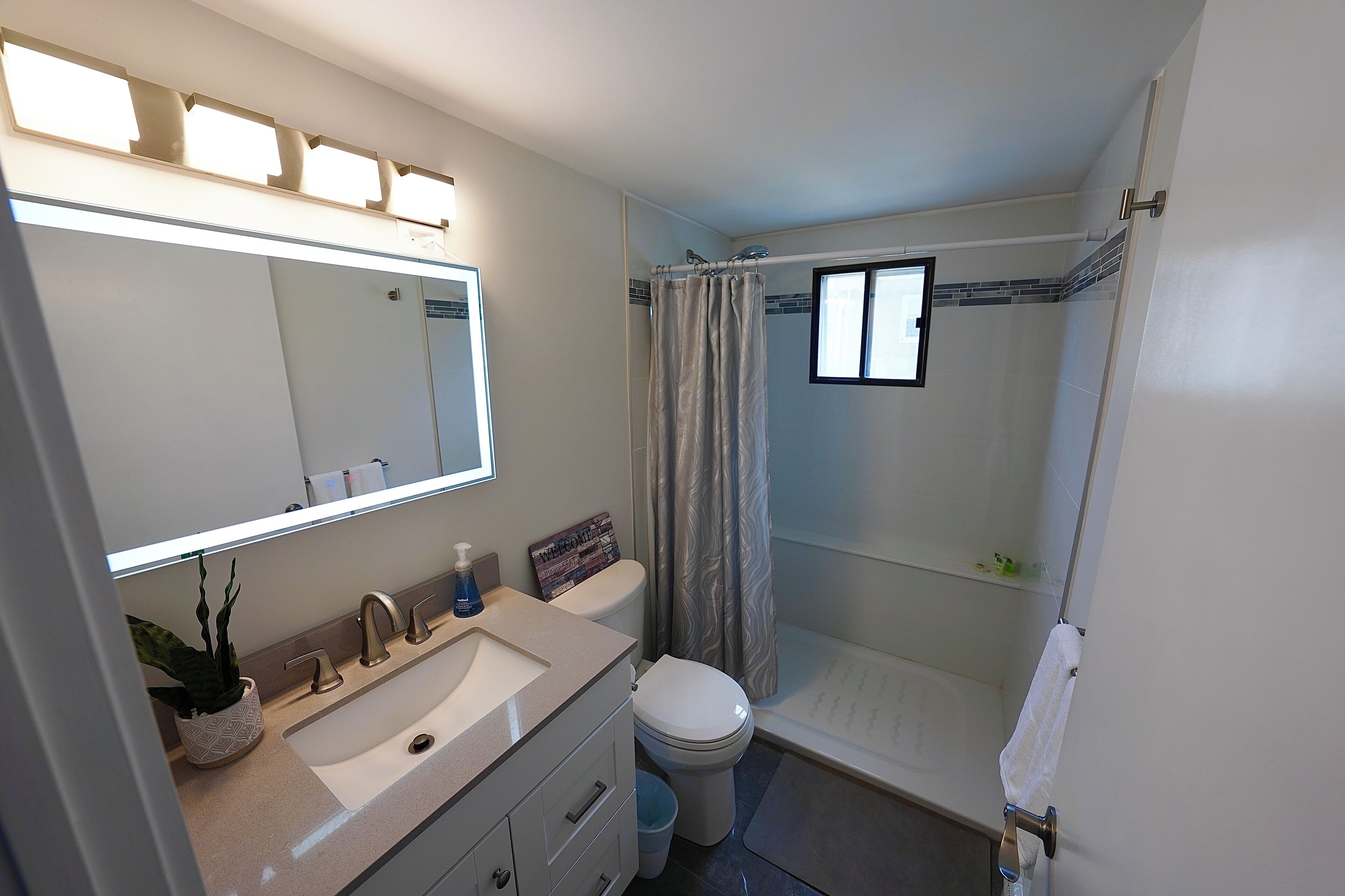 Un baño moderno con un espejo grande, un lavabo, un inodoro y una zona de ducha.