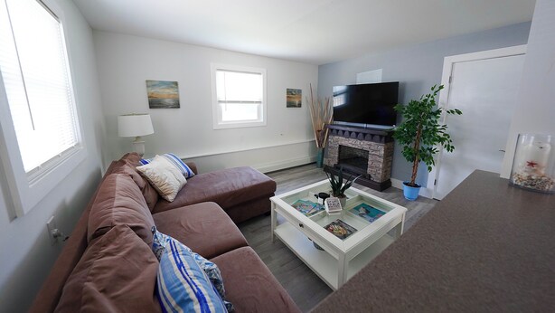 A living room with a brown sofa, a white coffee table, a flat-screen TV, a fireplace, and a potted plant.
