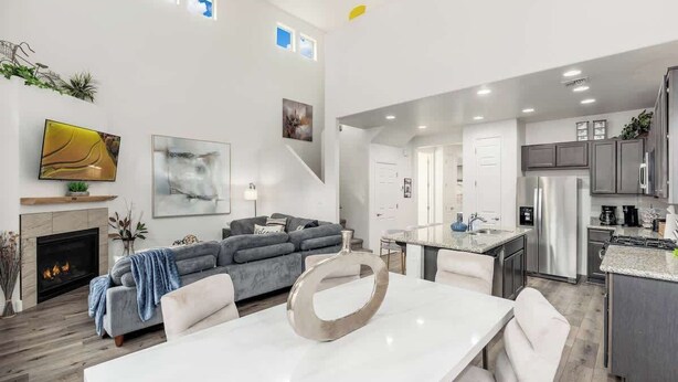 A modern open-plan living and dining area with a fireplace, sofa, dining table, and kitchen cabinetry.