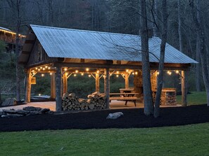 A wooden gazebo with a metal roof, string lights, and picnic tables.