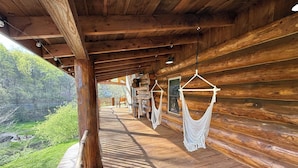 Uma cabana de madeira com varanda coberta, paredes de toras e vista para uma área arborizada.