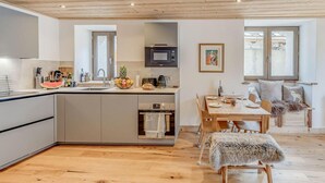 Une cuisine moderne dotée d’un îlot central, d’un coin repas avec une table et des chaises en bois, et d’un espace salon confortable agrémenté d’un plaid en fourrure.