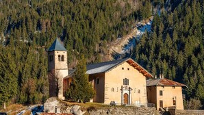 Une église dotée d’un clocher et d’un bâtiment principal, entourée d’une forêt dense et de montagnes.