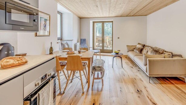 Une cuisine moderne dotée d’un four à micro-ondes encastré, un coin repas avec des chaises en bois et un canapé offrant une vue sur l’extérieur.