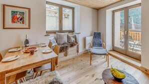 Un coin repas chaleureux avec une table en bois dressée pour deux personnes, une chaise confortable et une vue sur l’extérieur grâce à de grandes fenêtres.