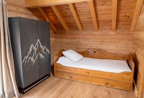 A wooden cabin room with a bed, a cabinet with a mountain design, and a wooden ceiling.
