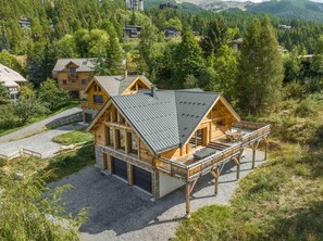A wooden cabin with a deck, surrounded by forested hills.