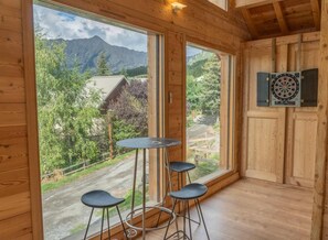 A wooden room with a large window, a dartboard, and a small table with stools.