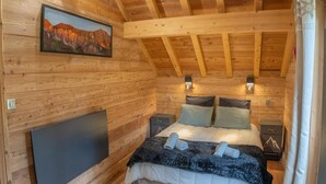 A wooden cabin bedroom with a bed, bedside tables, a mounted TV, and a mountain painting on the wall. - 350m from ski slopes, view mountain, balcony, tv, ski locker, 153m², Les Orres (Les Orres)