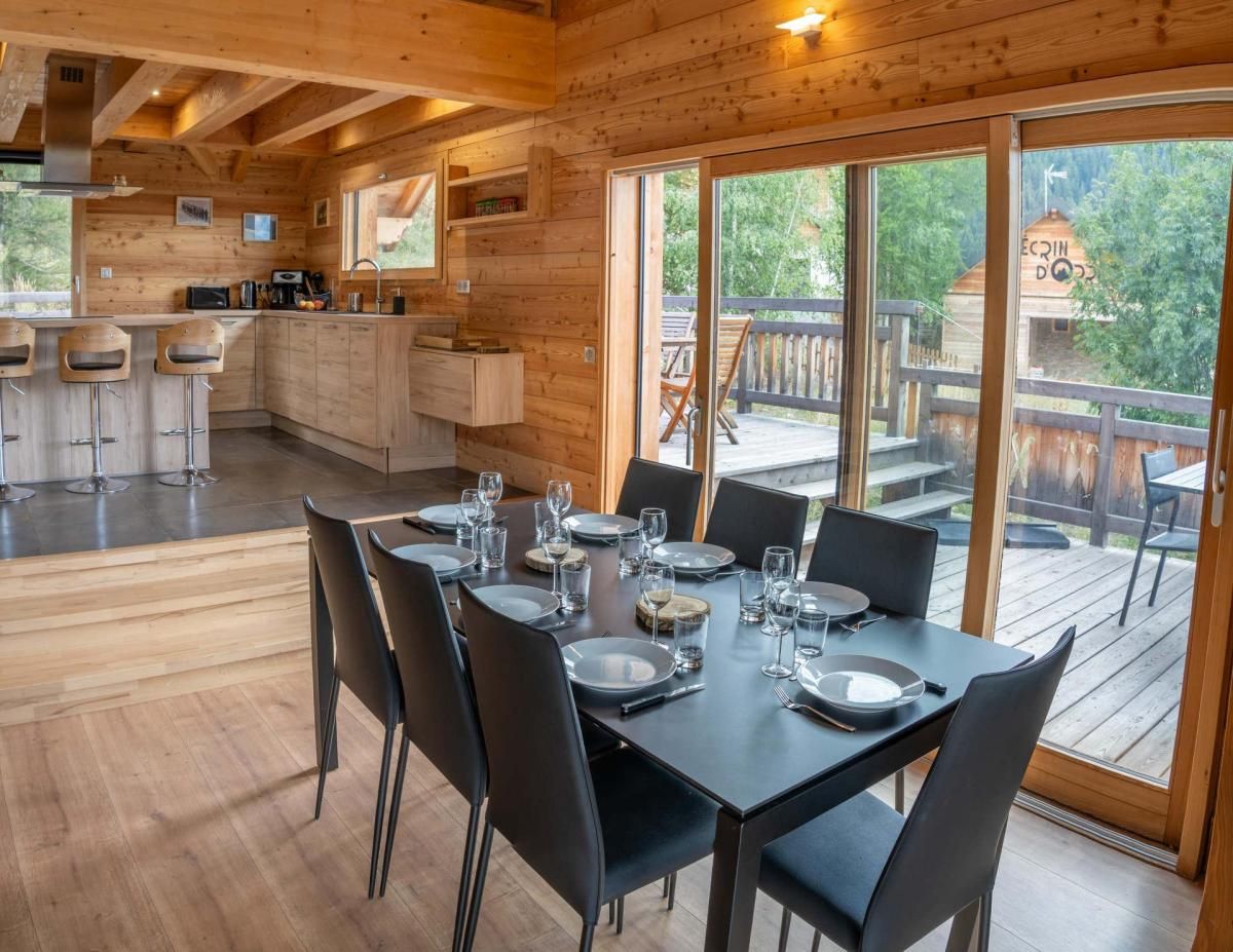 Eine Holzhütte mit Essbereich für sechs Personen, einer Küche mit Barhocker und einer Terrasse mit Sitzgelegenheiten.