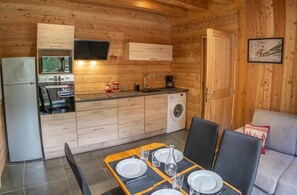 A compact kitchen with a refrigerator, microwave, sink, and a washing machine. There is a dining area with a table set for two.