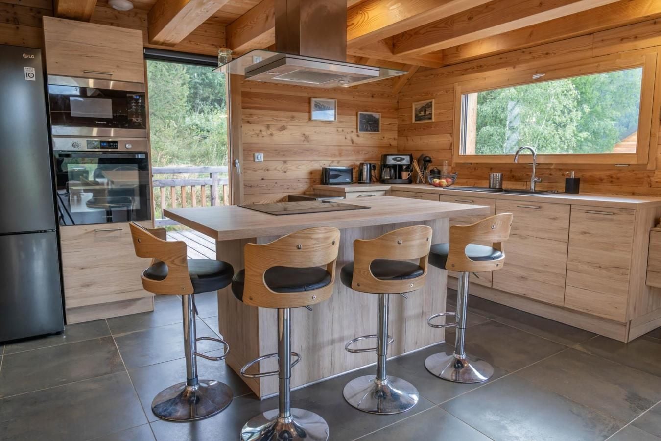 Una cocina moderna con una isla central, taburetes de bar, electrodomésticos de acero inoxidable y armarios de madera.