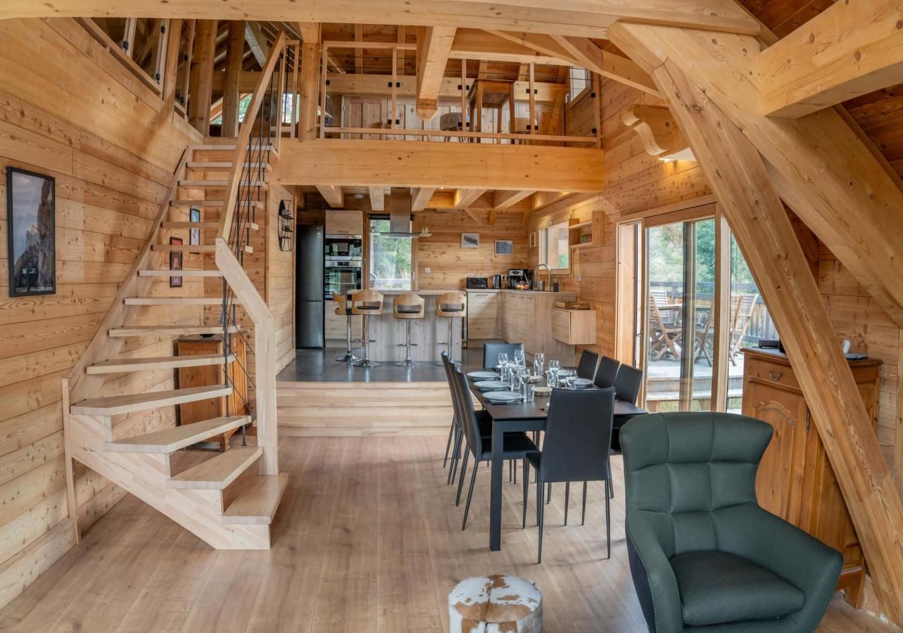 L’intérieur d’un chalet en bois comprend un escalier, un coin repas, une cuisine et de grandes fenêtres.