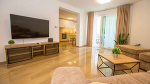 A modern living room with a flat-screen TV, a wooden entertainment unit, a dining area with a kitchen, and a balcony with curtains.