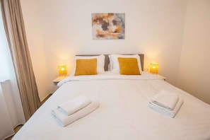 A hotel room with a large bed, two bedside lamps, a painting on the wall, and a window with curtains. - Holiday flat directly on the promenade (Poreč)