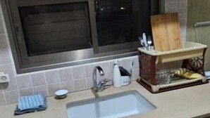 A kitchen with wooden cabinets, a microwave, a sink, and a small dining area with a chair.