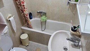 A bathroom with a toilet, sink, bathtub, shower, and a window.