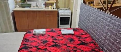 Une petite chambre comprenant un lit, une kitchenette et une petite fenêtre.