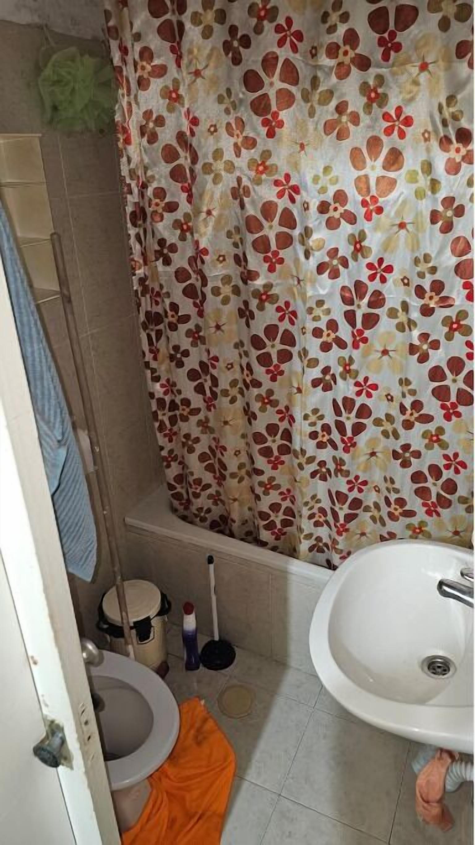 A bathroom with a toilet, sink, shower curtain, and cleaning supplies.