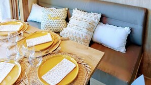 A cozy room with a wooden ceiling, a sofa with cushions, a dining table set with yellow plates and glasses, and a shelf with decorative items. - LE DOMAINE DE LA RICHE (Bioussac)