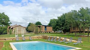 A swimming pool with lounge chairs, a stone building, and wooden structures in a landscaped area. - LE DOMAINE DE LA RICHE (Bioussac)