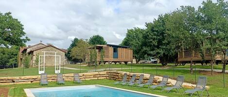 A swimming pool with lounge chairs, a stone building, and wooden structures in a landscaped area.