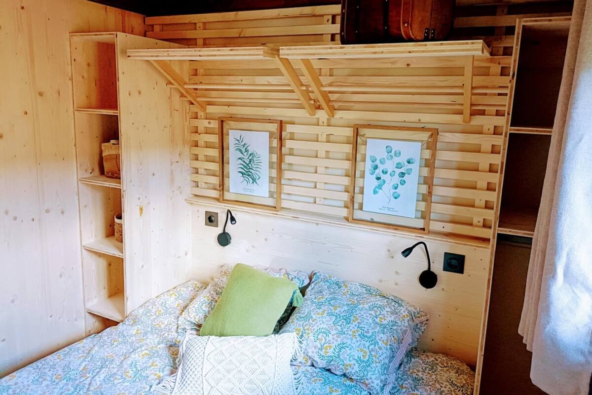 Ein Zimmer aus Holz mit einem Bett, Regalen und gerahmten Pflanzenbildern an der Wand.