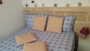 Un dormitorio con una colcha estampada, dos almohadas, un cabecero y una mesita de noche con una lámpara.