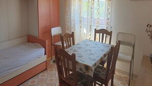 Una habitación pequeña y acogedora con una cama individual, una mesa con sillas y una ventana con cortinas.
