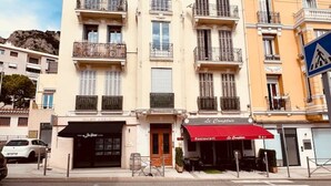 A multi-story building with balconies, a restaurant with a red awning, and a pedestrian crossing sign.