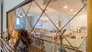 Un coin repas agrémenté d’un lustre, une cuisine avec un évier et un miroir décoratif doté d’un cadre géométrique.