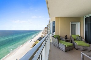 Een balkon met rieten meubels, uitzicht op het strand en een gebouw op de achtergrond.