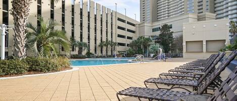 A poolside area with lounge chairs, a swimming pool, and a building with multiple floors and balconies.
