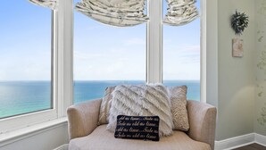 Un coin salon confortable avec vue sur l’océan, un coussin décoratif orné d’une citation et un mur agrémenté d’une œuvre d’art encadrée.