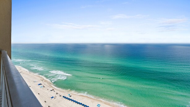 Une vue sur la plage depuis un balcon, avec un ciel dégagé et une eau turquoise.