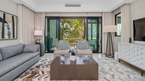 Una sala de estar moderna con un sofá gris, dos sillones, una mesa de centro y un televisor sobre un mueble blanco.