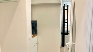 Ein schmaler Flur mit Holzboden, weißen Wänden und einer kleinen Bank mit einem zusammengerollten Gegenstand.