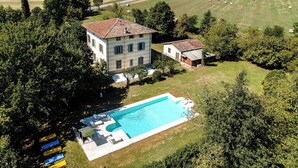 A large house with a swimming pool, surrounded by fields and trees.