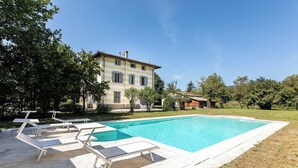 A swimming pool with lounge chairs, a large building with shutters, and a grassy area.