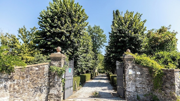 A stone pathway leading to a gated entrance with a number '6' sign, surrounded by lush greenery.